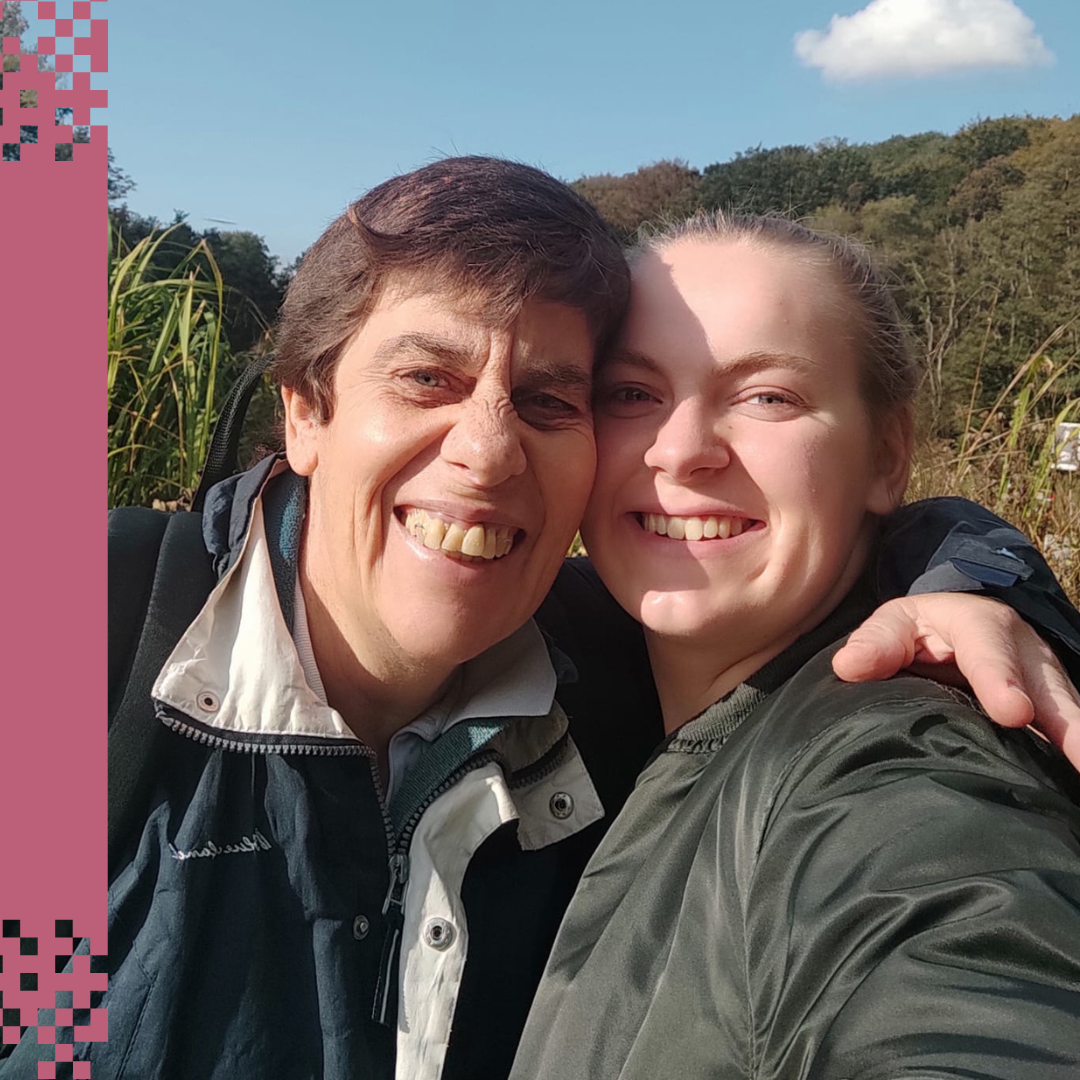 Louisa ist rechts im Bild und umarmt eine älere Frau. Die beiden schauen für das Selfie direkt in die Kamera.